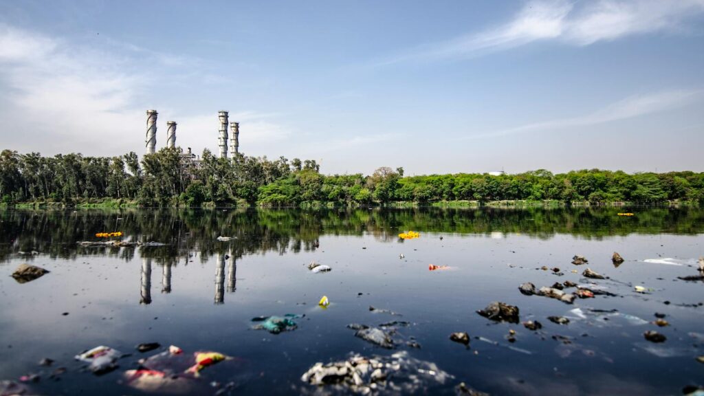 View of a polluted river reflecting factory emissions under a clear sky in India.