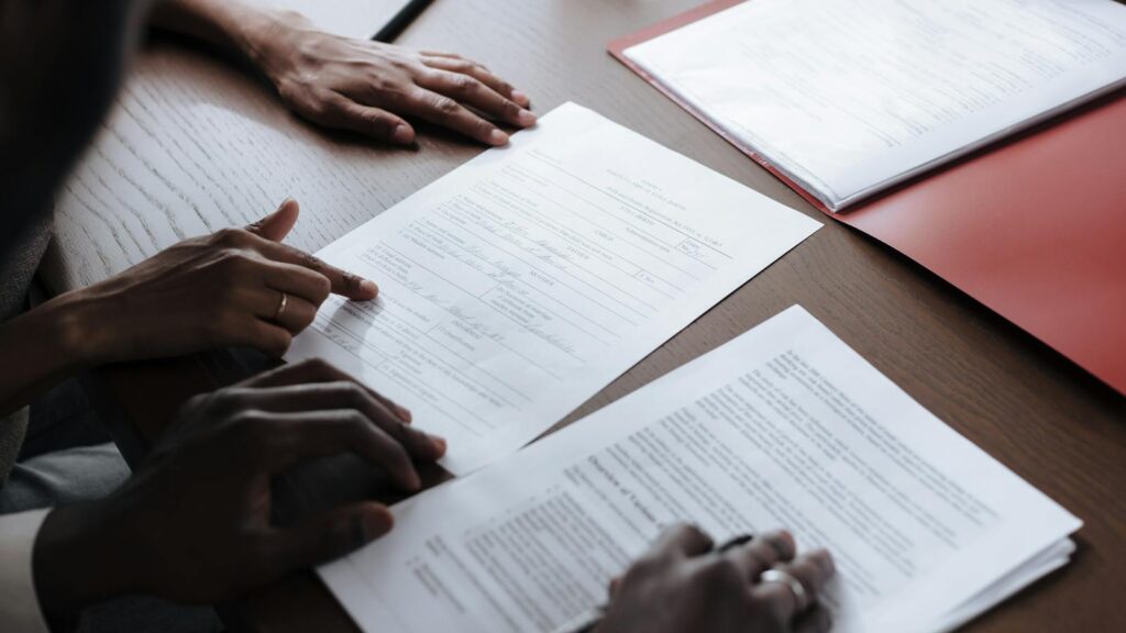Two individuals reviewing and signing official documents in an indoor setting.