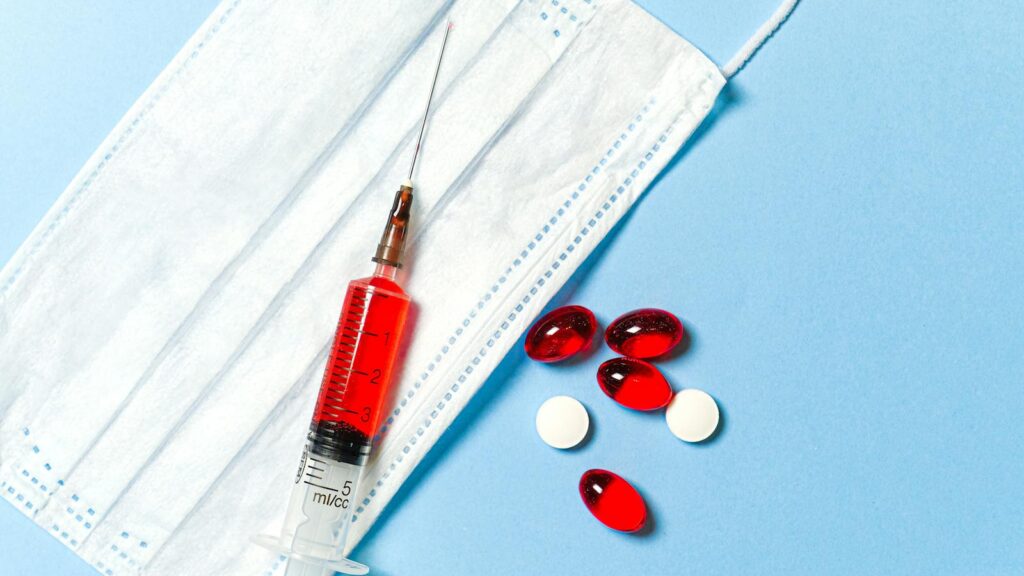 A syringe, face mask, and pills on a blue surface, symbolizing medical treatment.