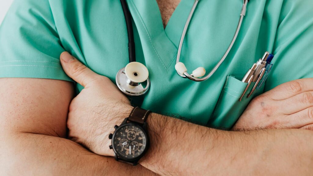 Close-up of a healthcare professional with arms crossed wearing medical scrubs and stethoscope.