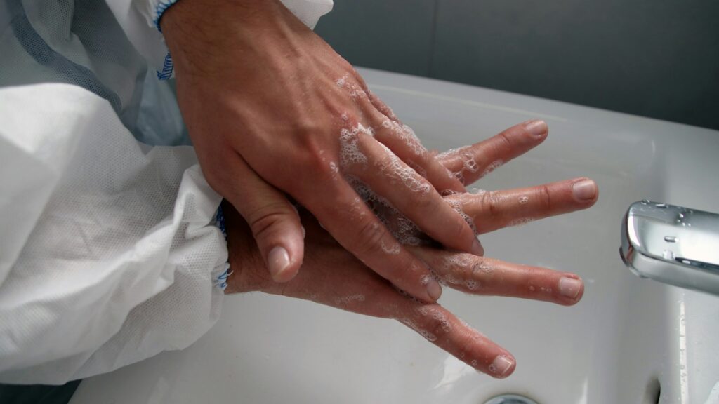 Hands being thoroughly washed with soap in a white sink.