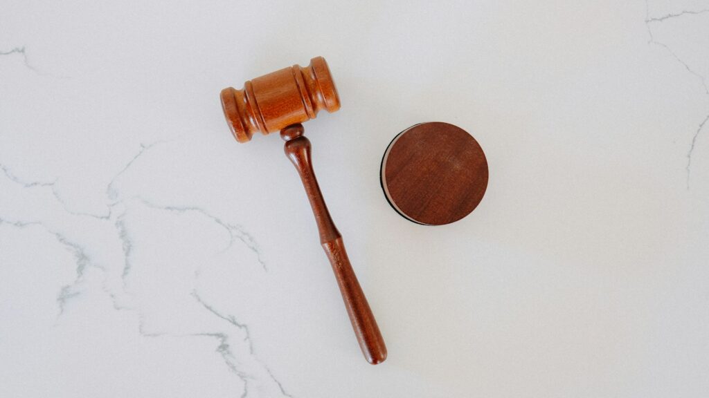 A wooden gavel rests beside its circular sound block on a white marble surface.