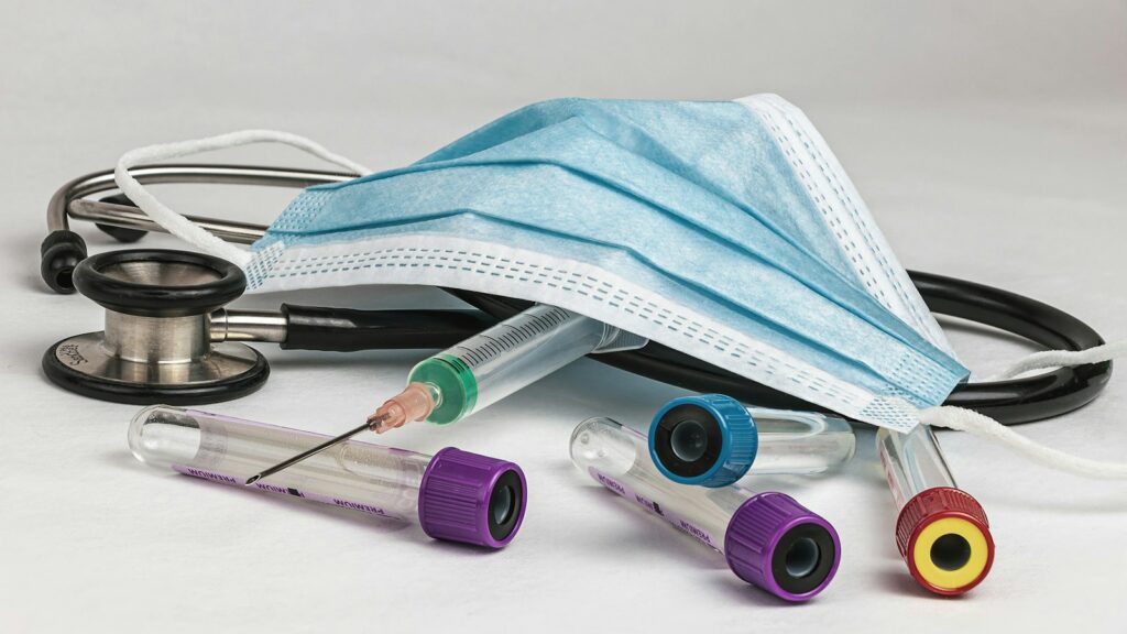 Medical equipment including a stethoscope, a syringe, blood test tubes, and a surgical mask on a white background.