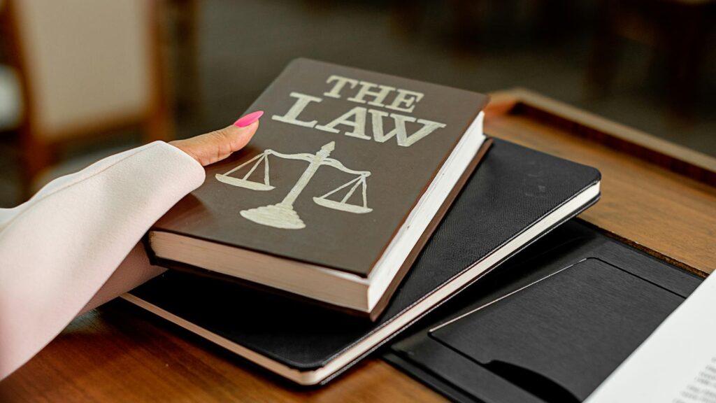Closeup image of a law book titled 'The Law' on a wooden desk with scales of justice.