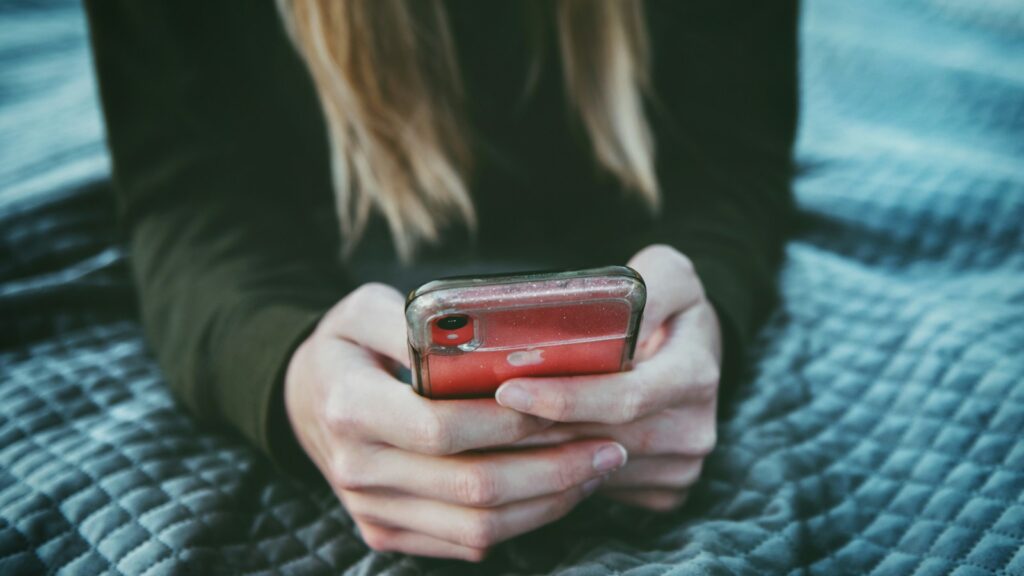 A woman with long blonde hair using her phone while lying on a textured blanket.