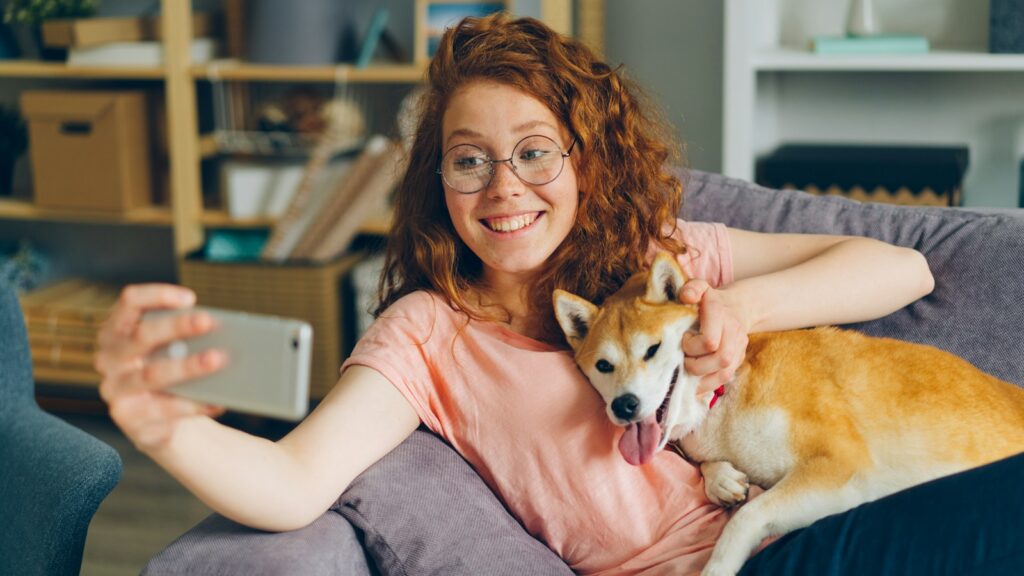 A woman sitting on a couch holding a dog and a phone.