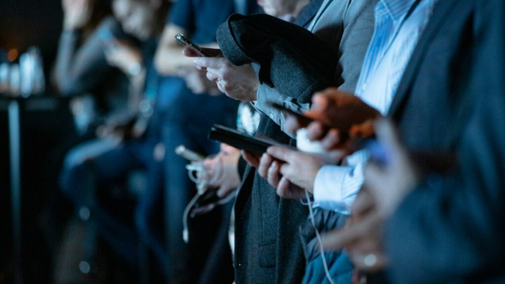A group of individuals absorbed in smartphones in a dark indoor setting.