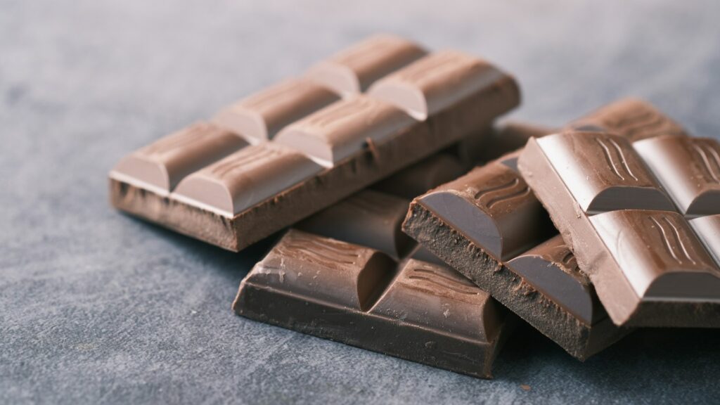 Several pieces of chocolate bars stacked on a textured gray surface.