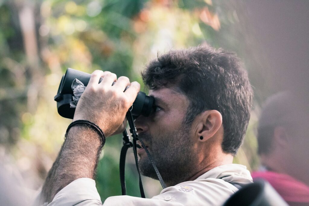 man using black binoculars at daytime to watch birds